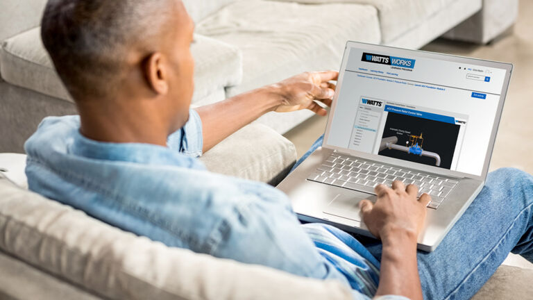 Man sitting on a couch in his home completing watts online training on his laptop 
