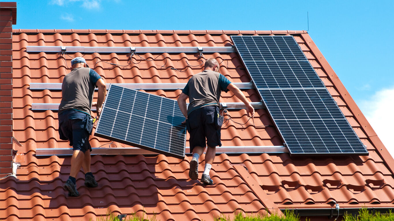 Two men installing solar panels on roof.